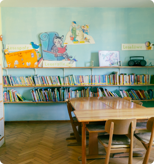Ruhige Leseecke mit Holzstühlen und -tisch vor einem Wandregal voller Kinderbücher.
